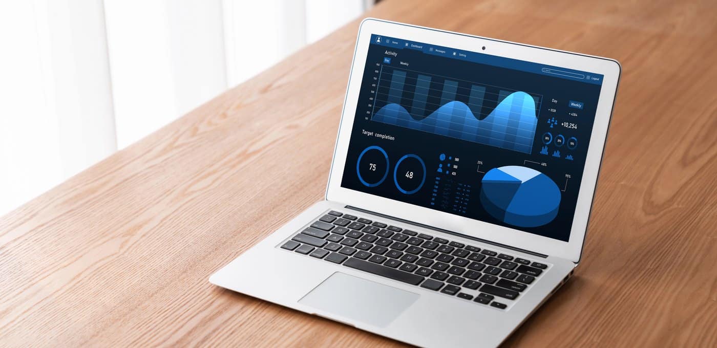 An open laptop on a wooden desk in daylight, showing a blue performance dashboard.